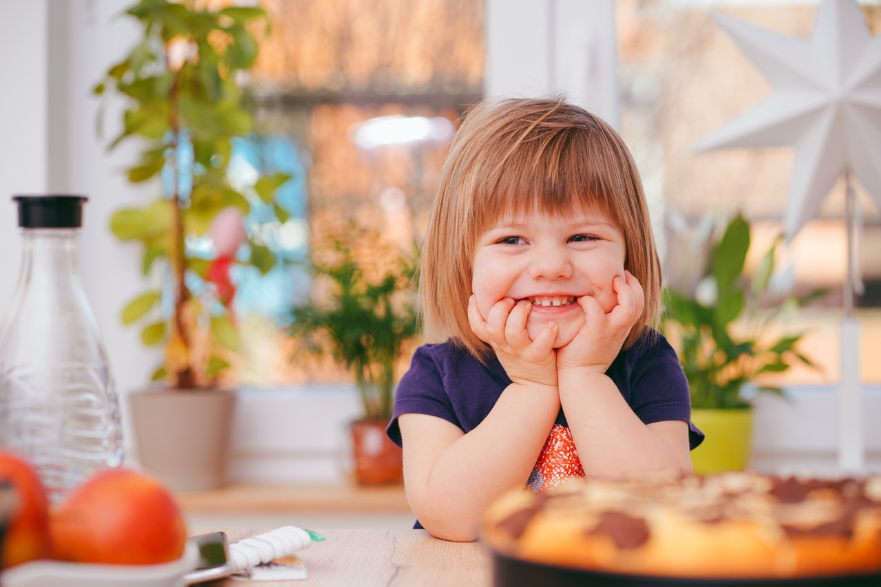 A little blond girl smiles in her parent's kitchen.
